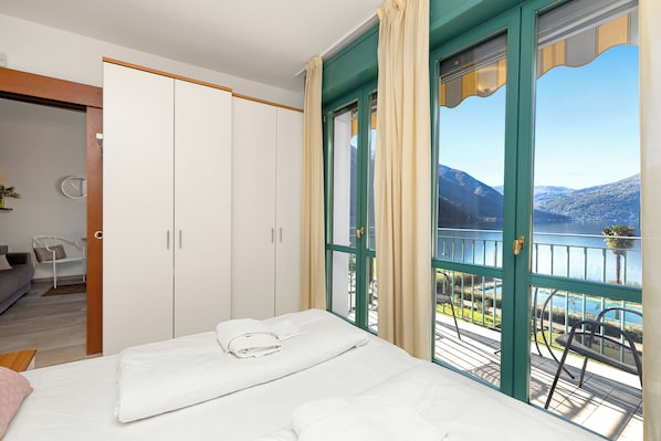 Une chambre à coucher comprenant un lit, une armoire et un balcon avec vue sur un lac et des montagnes.