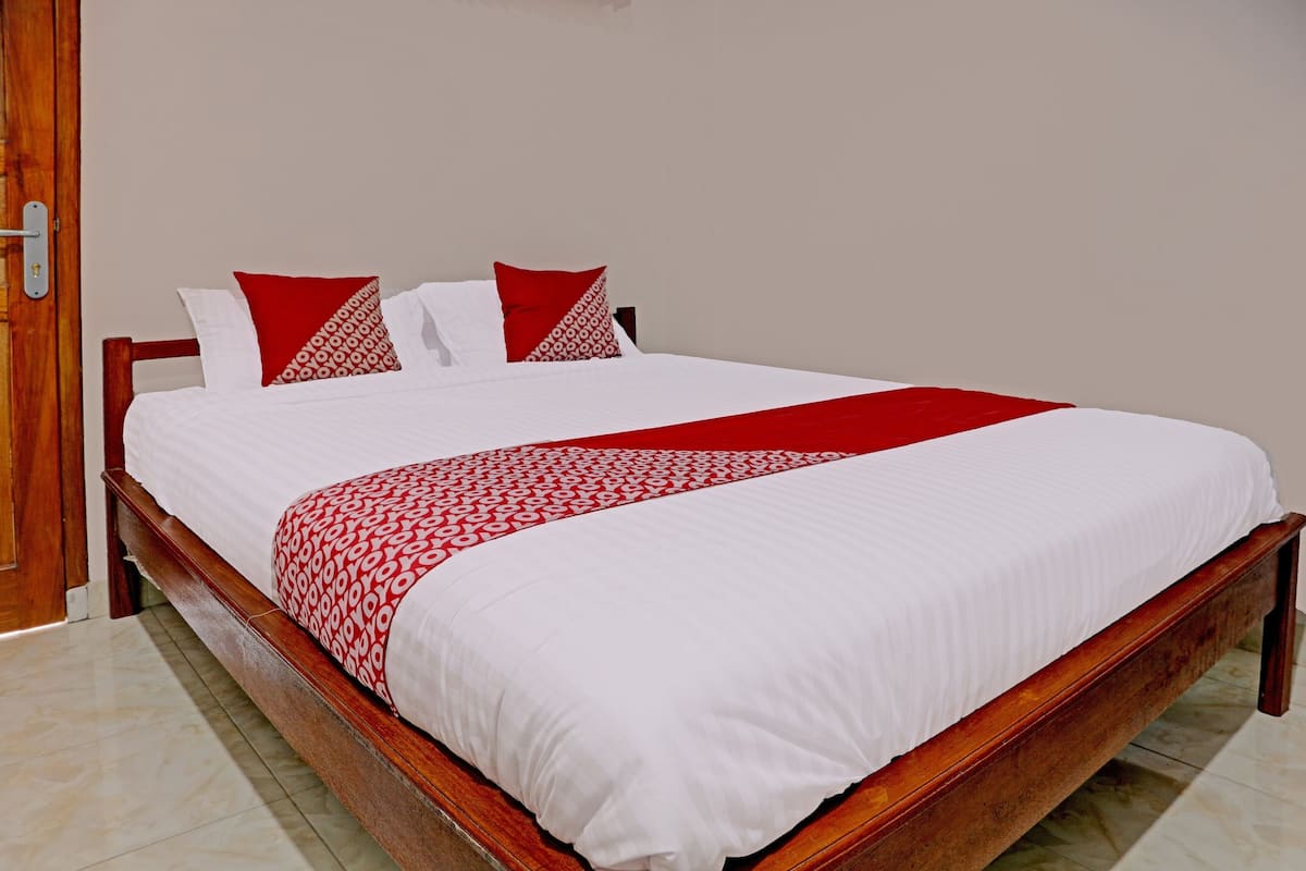 A neatly made bed with a white and red patterned bedspread and pillows, a wooden headboard, and a tiled floor.
