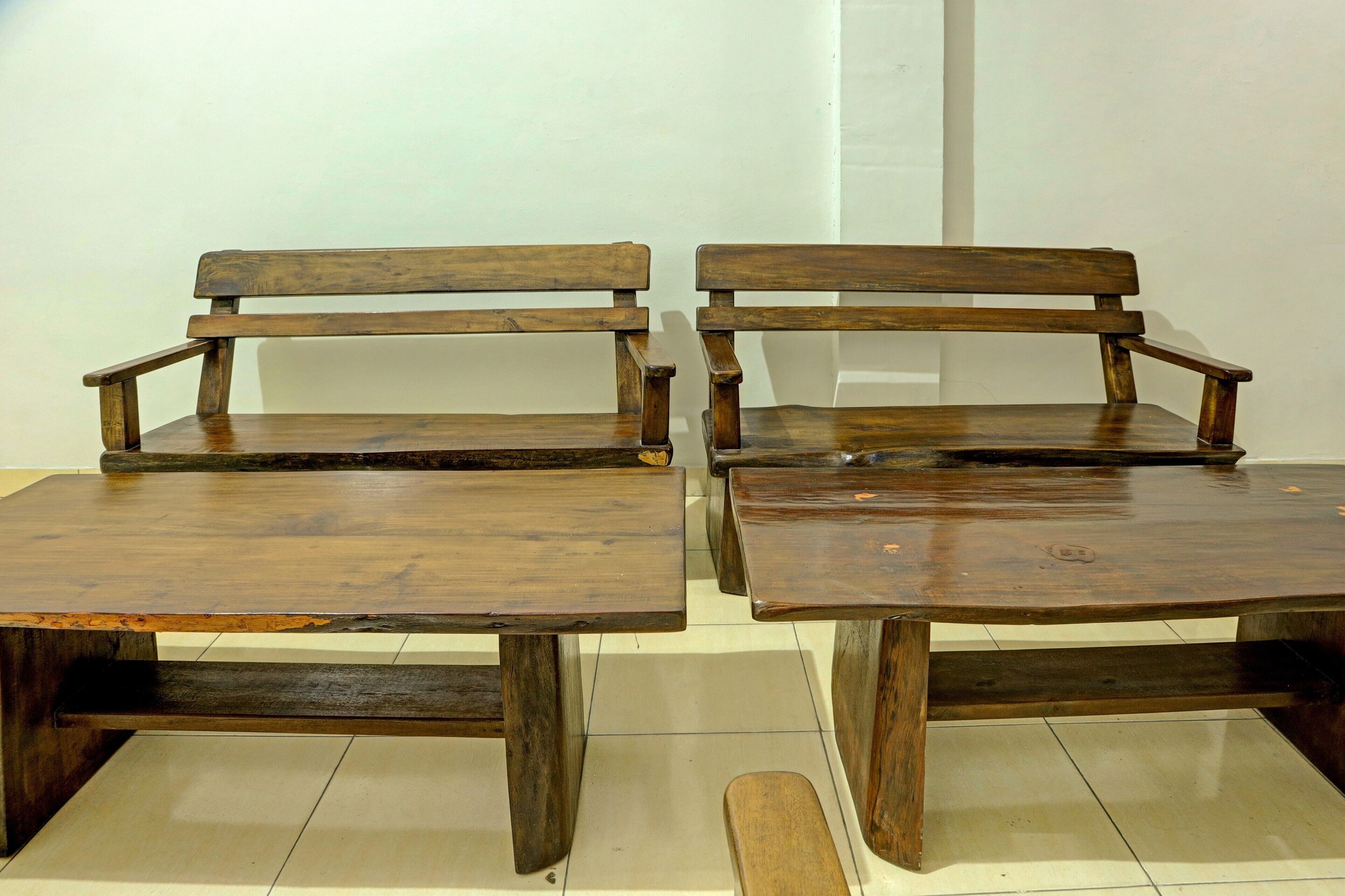 Dois bancos e mesas de madeira numa divisão com paredes brancas e chão em mosaico.