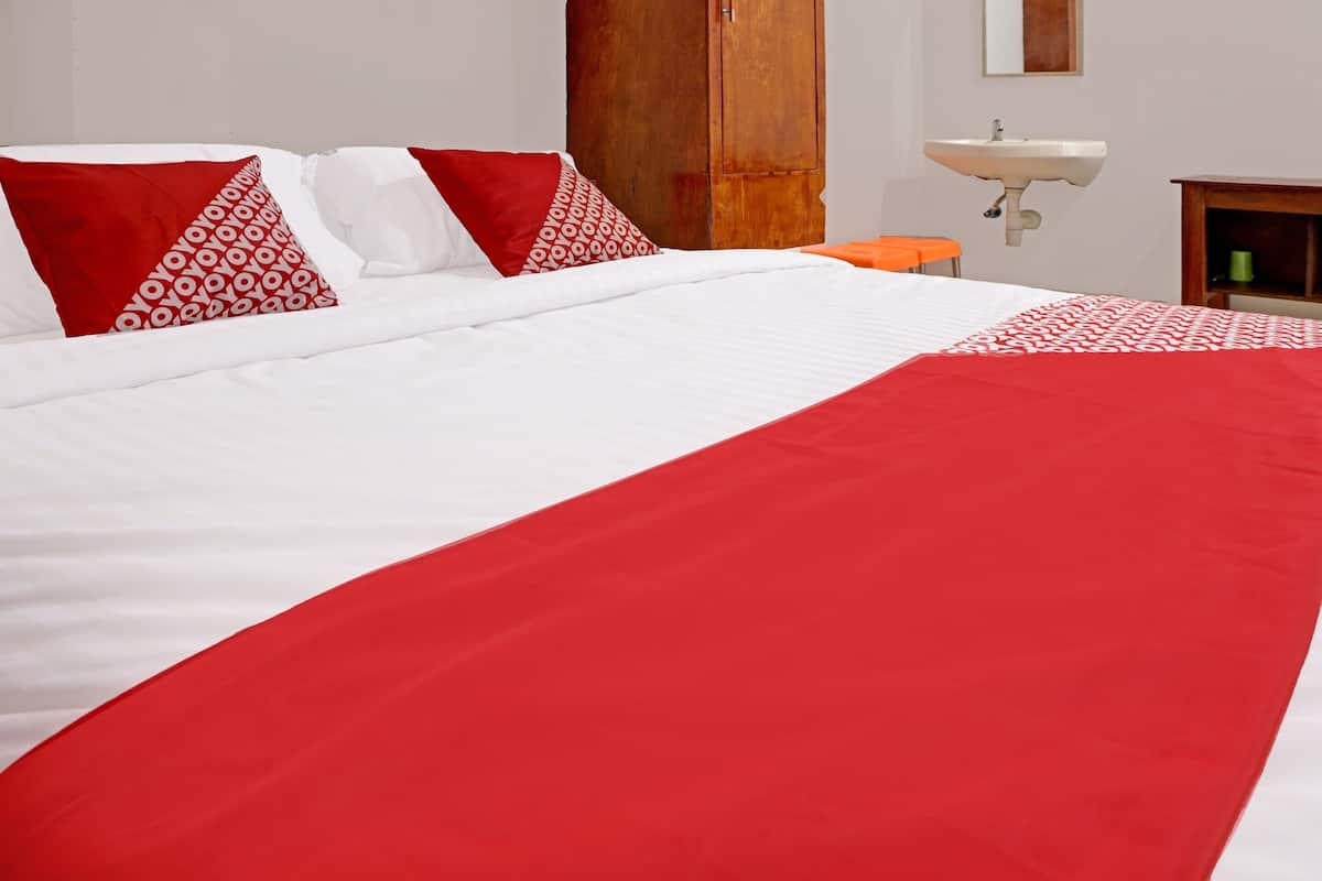 A hotel room with a large bed, a wooden wardrobe, a sink, and a small orange stool.
