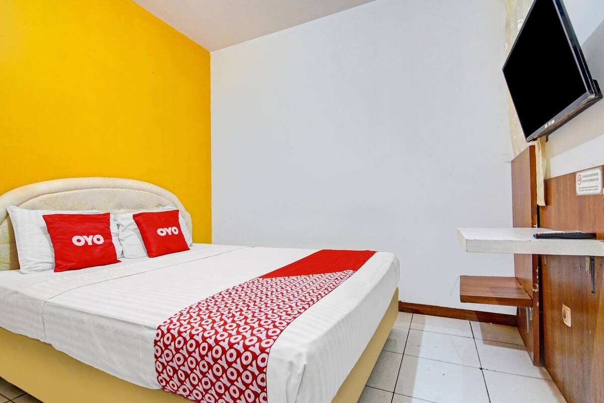 A hotel room with a bed, a TV mounted on the wall, and a wooden desk.