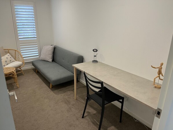 A small, well-lit room with a grey sofa, a wooden chair, a small table, and a wooden mannequin.