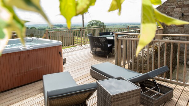 A wooden deck with a hot tub, lounge chairs, and a table with chairs. - A cottage that sleeps 8 guests  in 4 bedrooms (Castle Carrock)