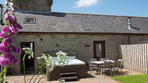 A stone building with a hot tub, outdoor seating, and a wooden fence. - A cottage that sleeps 6 guests  in 3 bedrooms (Castle Carrock)