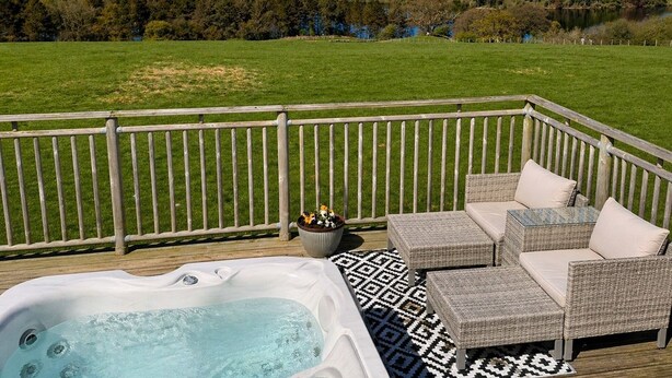 Um deck com hidromassagem, móveis de vime e vista para uma paisagem verde.