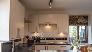Una cocina moderna con armarios blancos, encimera negra y ventana con vistas a zonas verdes.