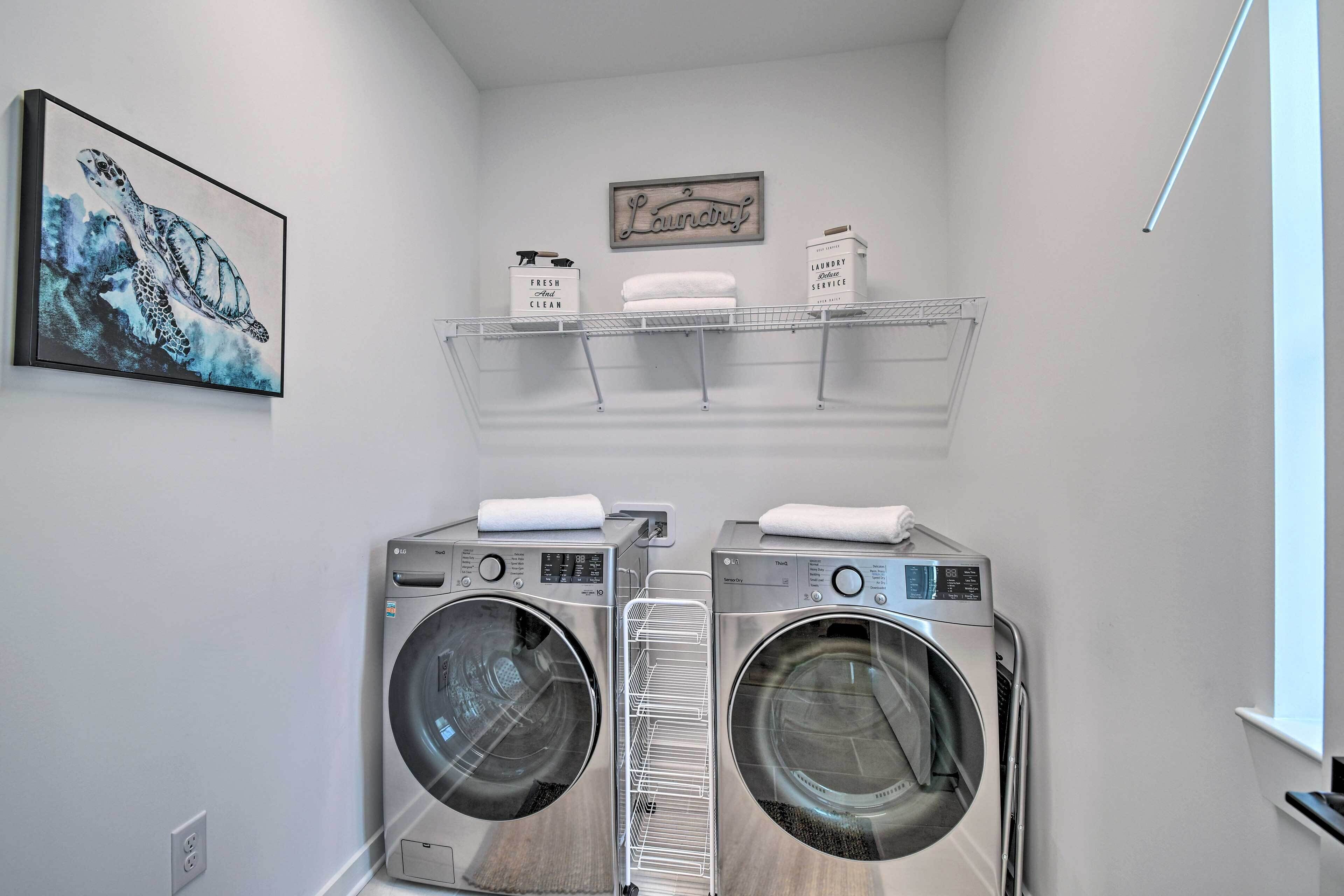 A laundry room with two stacked front-loading washers and dryers, a drying rack, and a framed artwork of a sea turtle.
