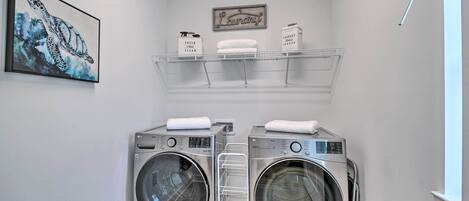 A laundry room with two stacked front-loading washers and dryers, a drying rack, and a framed artwork of a sea turtle.