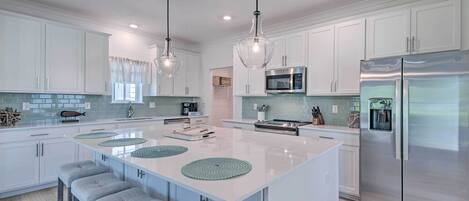 A modern kitchen with white cabinets, a central island with stools, stainless steel appliances, and pendant lighting.