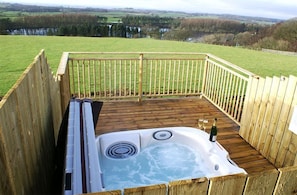 Relax on the elevated deck overlooking a serene landscape with a hot tub at your fingertips.