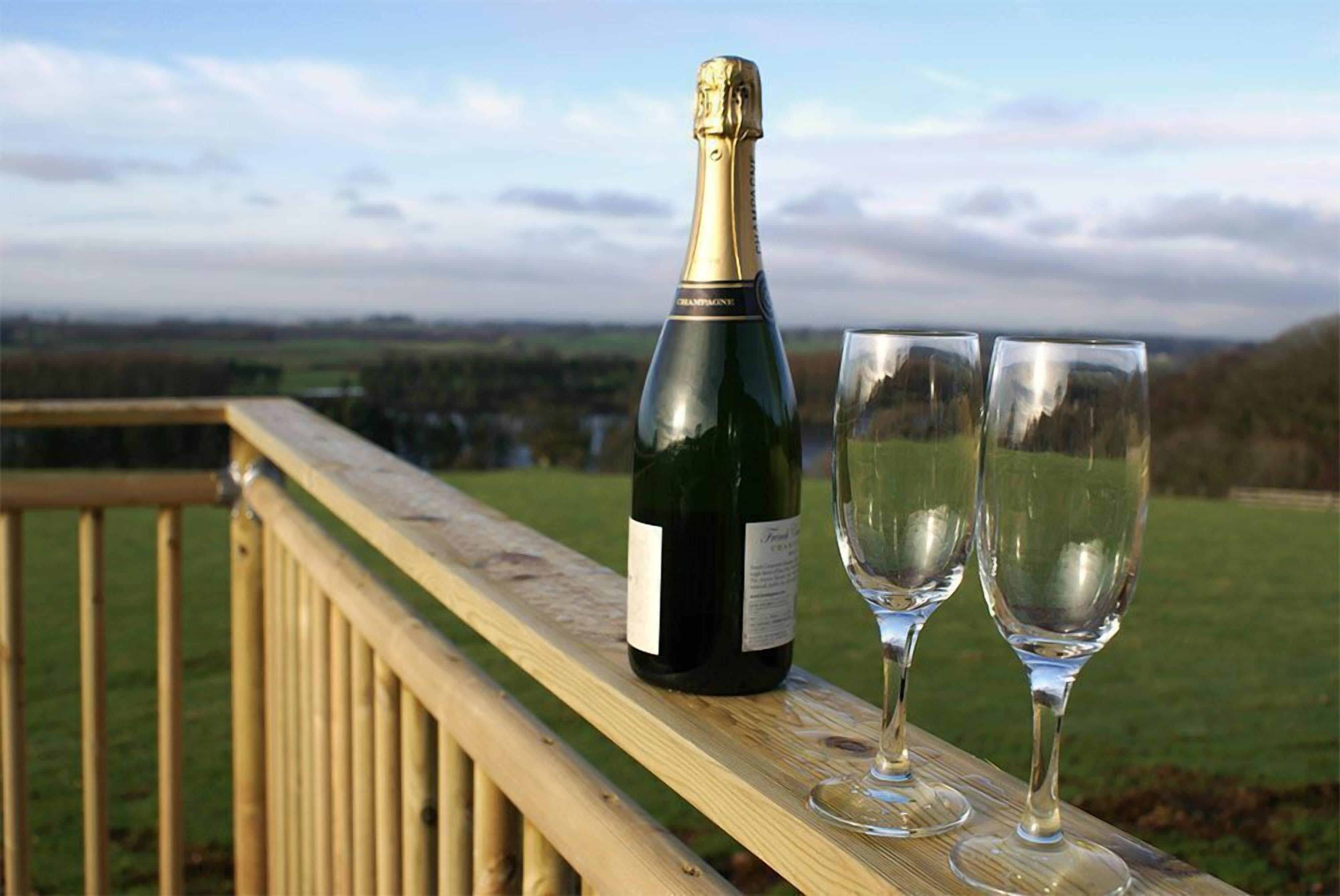 Eine Champagnerflasche und zwei Gläser auf einem Holzdeck mit Blick auf eine Landschaft.
