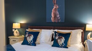 Ein Hotelzimmer mit einem großen Bett, zwei mit Hasen-Motiven versehenen Kissen, einem Kopfteil, Nachttischen mit Lampen und einem an der Wand hängenden Bild von einem Hasen.