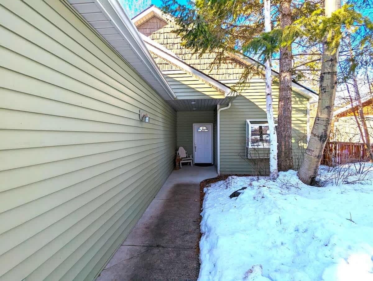 Un sendero estrecho que conduce a una puerta, un pequeño porche y suelo cubierto de nieve.