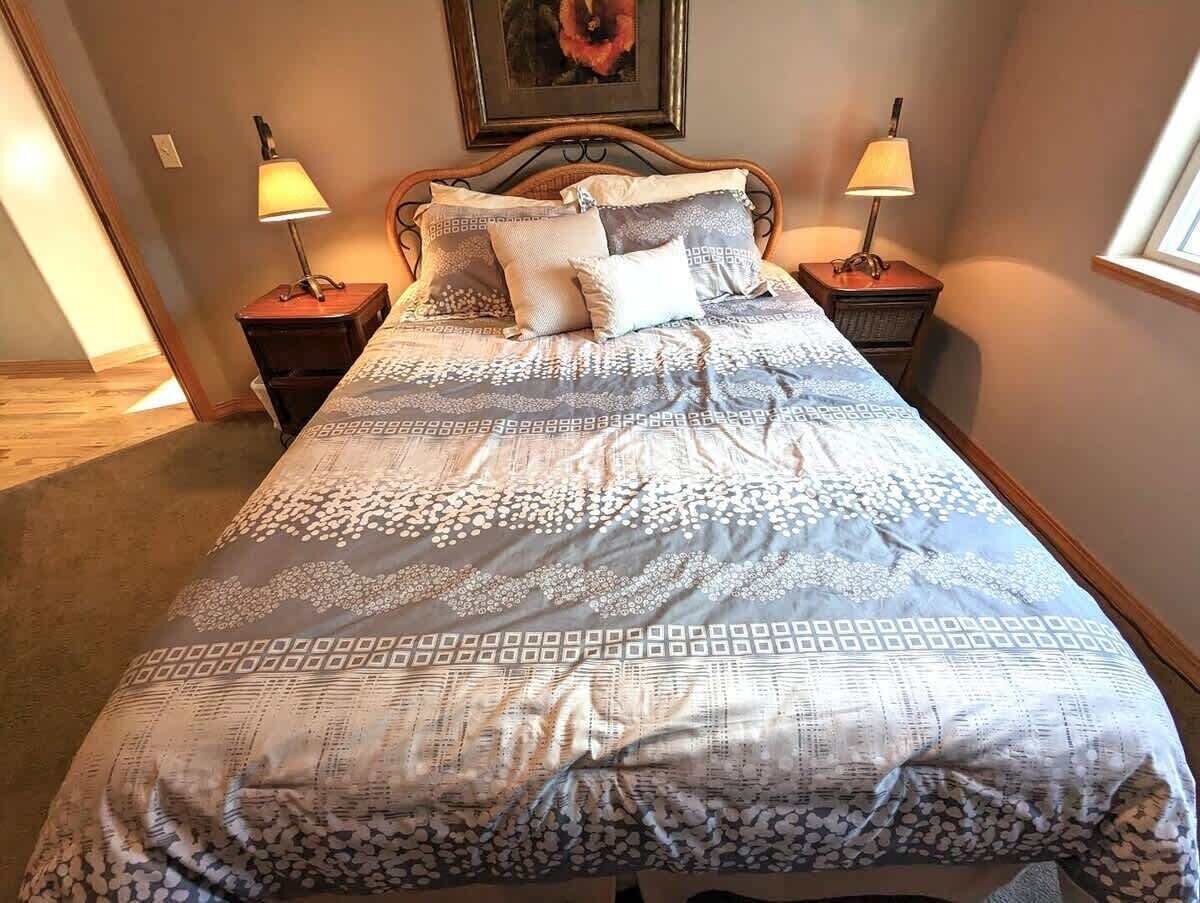 A neatly made bed with a patterned bedspread, two bedside lamps, and a framed picture on the wall.