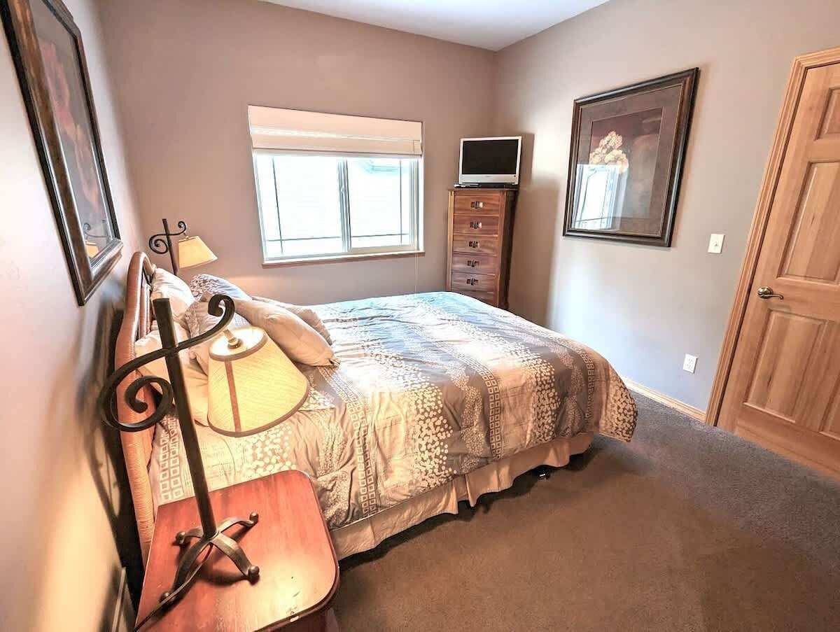 Une chambre à coucher avec un lit, une lampe, un téléviseur posé sur un meuble, une commode et une porte.