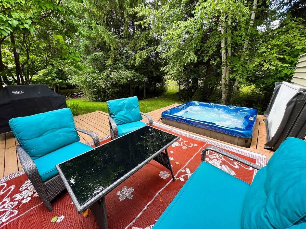 An outdoor patio with a hot tub, wicker chairs with blue cushions, and a glass table.