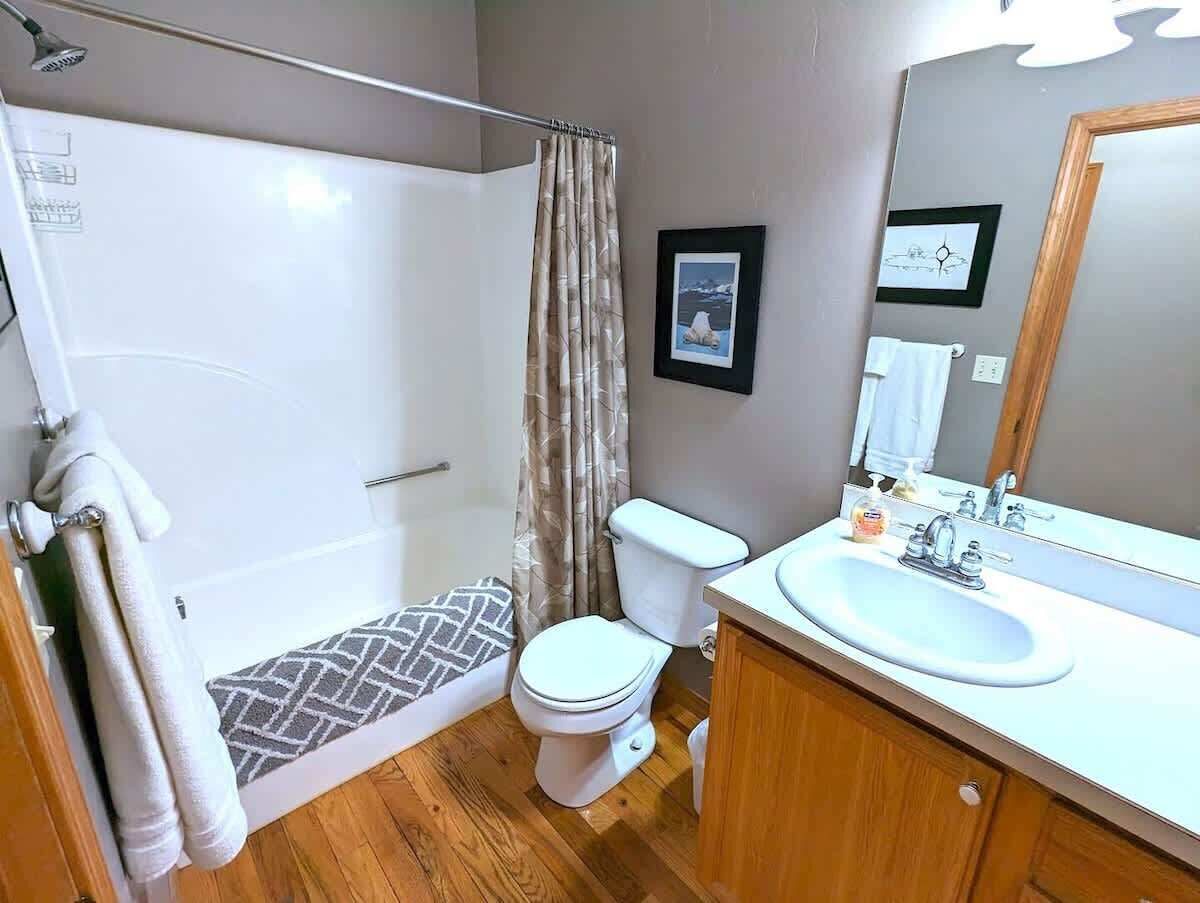 A bathroom with a shower, toilet, sink, and mirror.