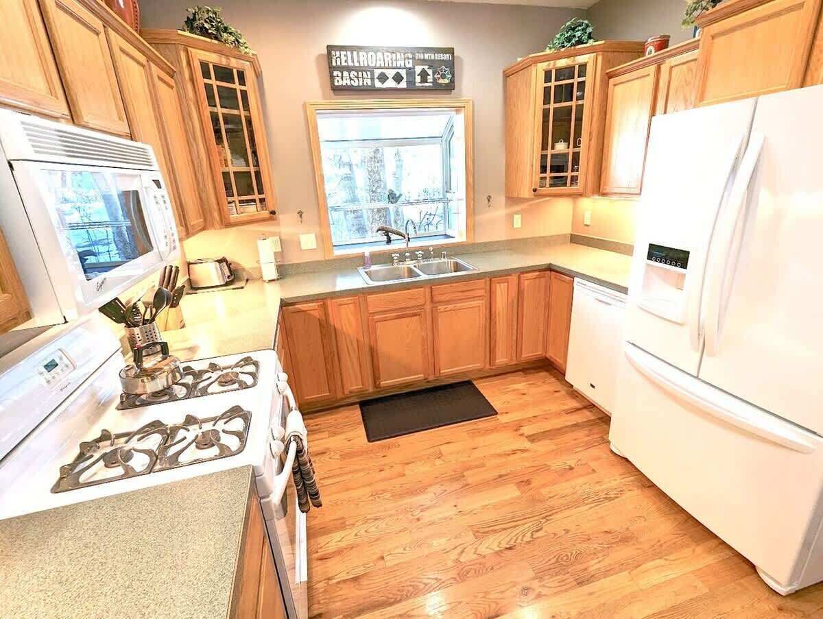 A kitchen with wooden cabinets, a white refrigerator, a stove, and a window with a view of trees.