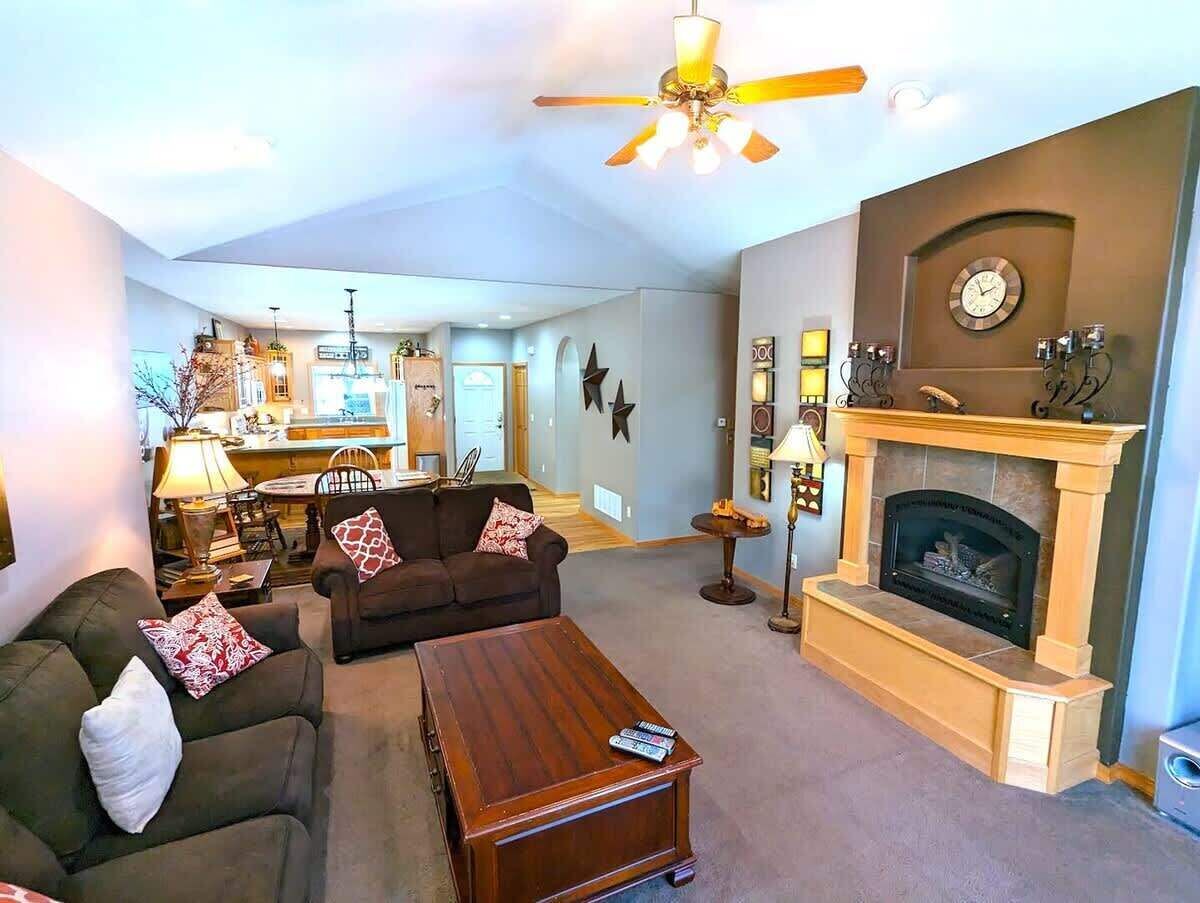 Una sala de estar con chimenea, ventilador de techo y una zona de comedor al fondo.