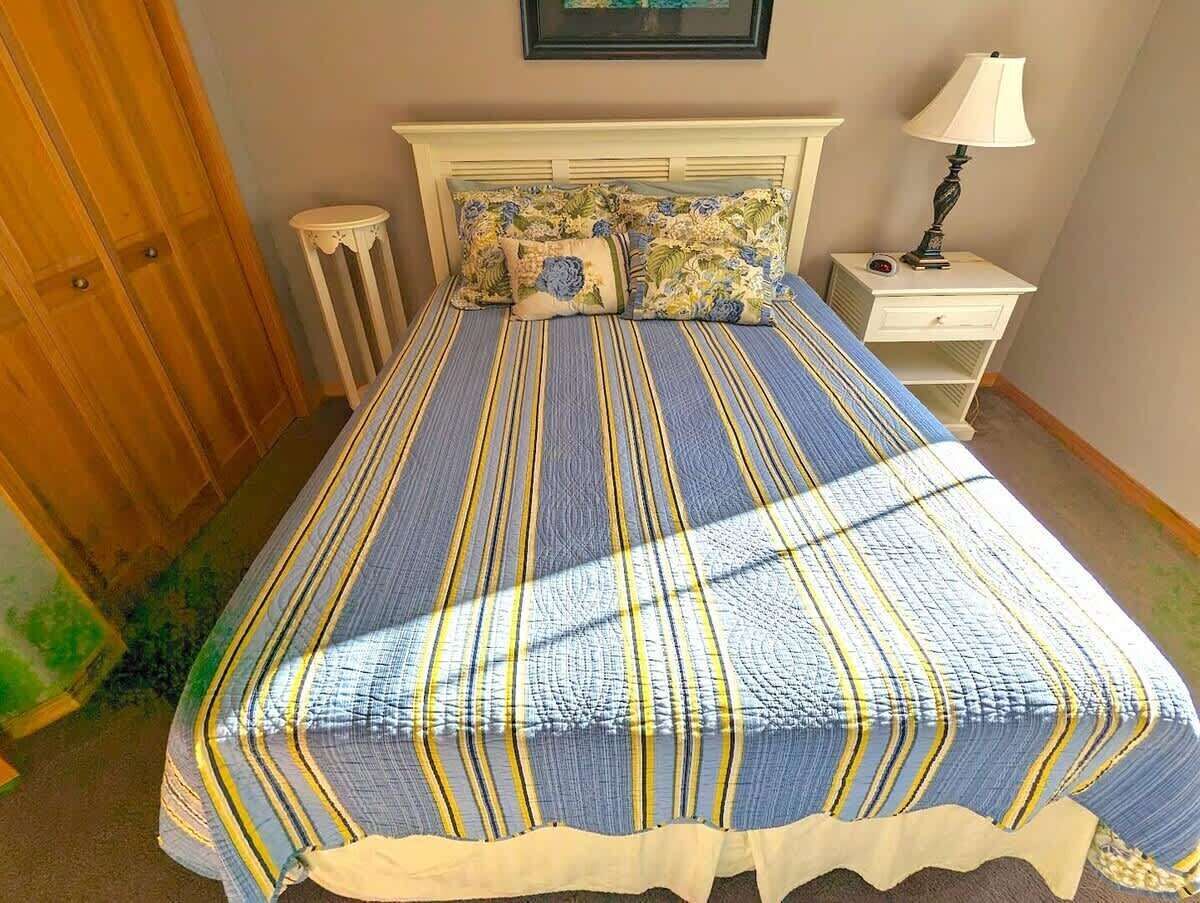 Een bed met een gestreept dekbed, een nachtkastje met een lamp en een klein krukje.