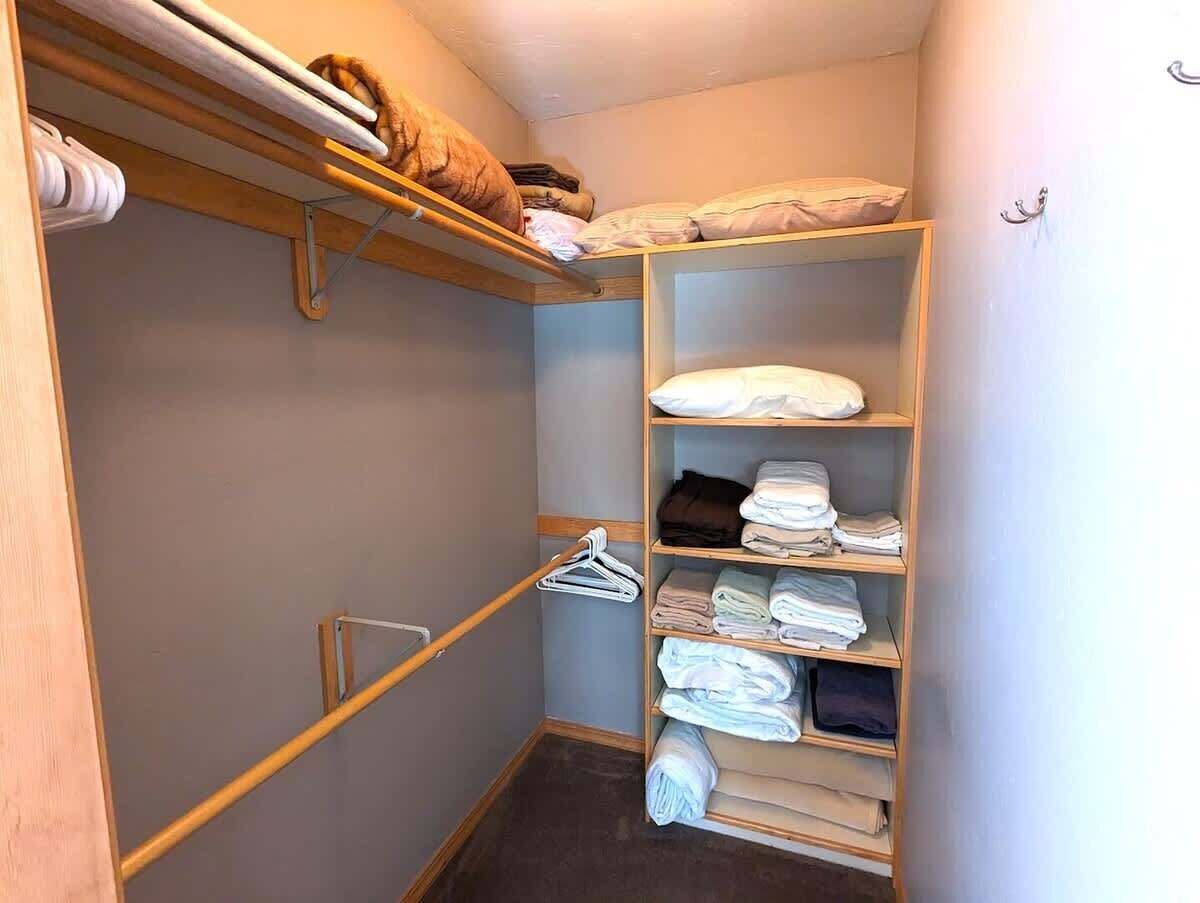 A small, narrow closet with wooden shelves, a hanging rod, and a metal hanger rack.