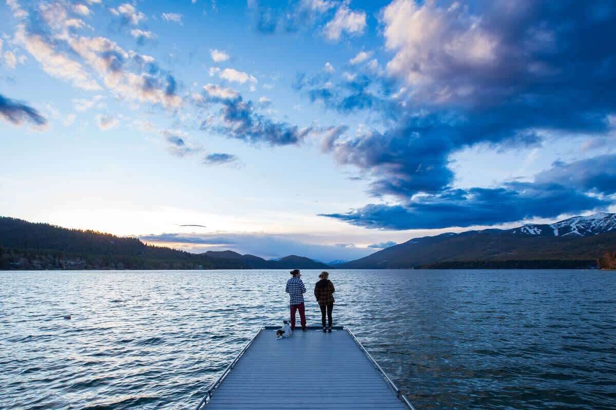 A wooden pier extending into a calm lake with mountains in the background.