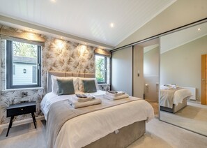 Quarto moderno com cama grande, mesa de cabeceira, espelho e porta deslizante para um banheiro.