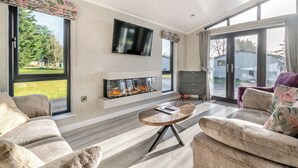 Un salon moderne doté d’une cheminée, d’un téléviseur à écran plat et de grandes fenêtres.