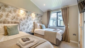 Une chambre avec deux lits, une fenêtre avec des rideaux, un téléviseur à écran plat et un mur décoré d’un motif.
