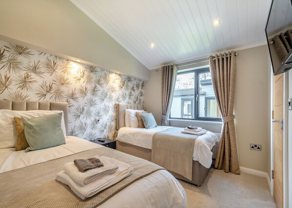 A bedroom with two beds, a window with curtains, a flat-screen TV, and a patterned wall.
