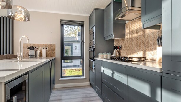 Une cuisine moderne dotée d’une grande fenêtre, d’appareils électroménagers en acier inoxydable et d’un dosseret en carreaux disposés en motif chevron.