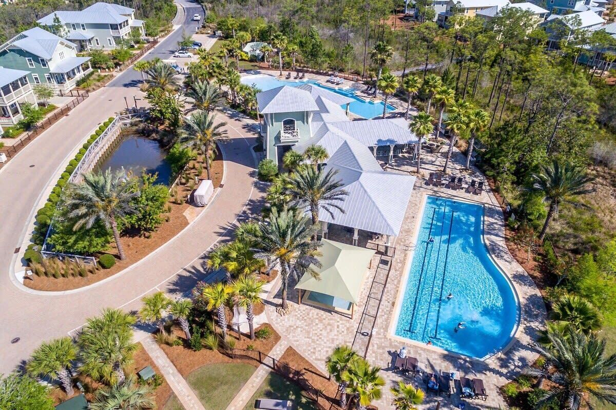 An aerial view of a resort with a swimming pool, palm trees, and a road.
