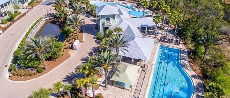 An aerial view of a resort with a swimming pool, palm trees, and a road.