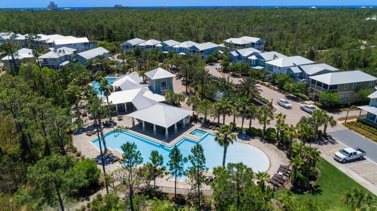 An aerial view of a resort with multiple buildings, a central pool area, and surrounding palm trees.