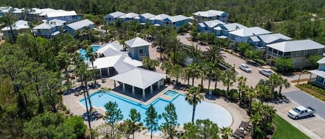 An aerial view of a resort with multiple buildings, a central pool area, and surrounding palm trees.