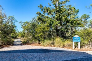 A paved pathway leading to a beach trail sign.