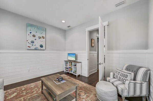 A living room with a television, a bookshelf, a coffee table, and a striped armchair.