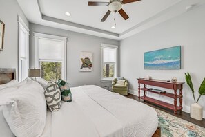 Une chambre à coucher avec un grand lit, un ventilateur de plafond, un tableau, une table de chevet et une fenêtre donnant sur un beau paysage.