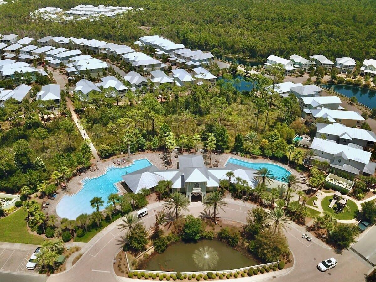 An aerial view of a resort with multiple buildings, a central pool, and surrounding greenery.