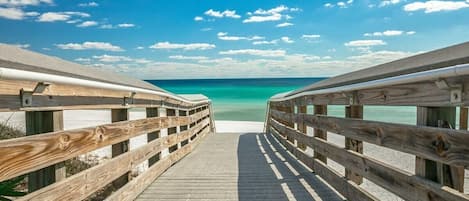 A wooden boardwalk leading to a beach with clear turquoise water and a clear sky.