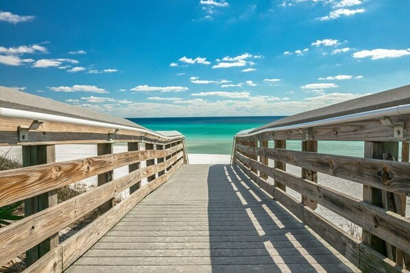 A wooden boardwalk leading to a beach with clear turquoise water and a clear sky.