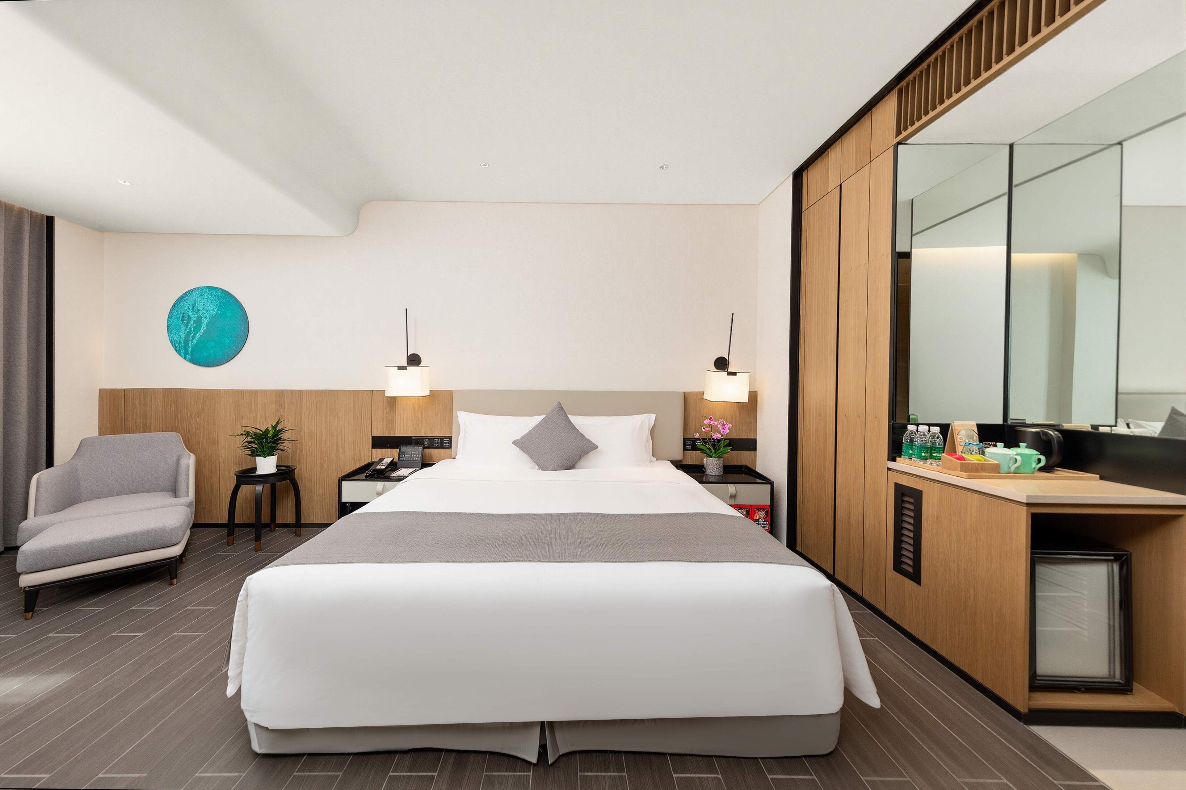 Een moderne hotelkamer met een groot bed, een bureau met spiegel, een stoel en een kleine tafel met een plant.