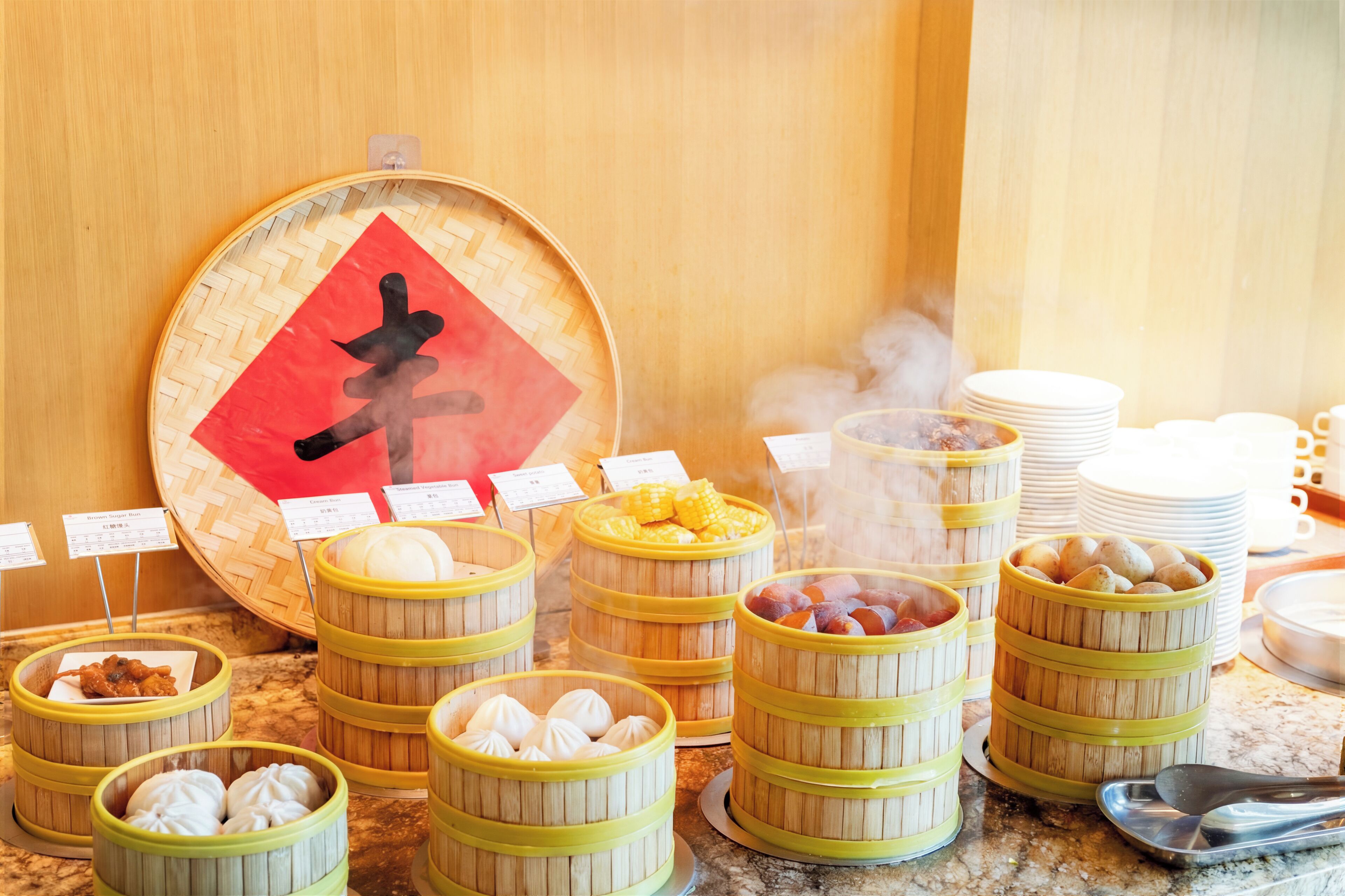 A buffet with various food items in bamboo steamers, including dumplings and corn.