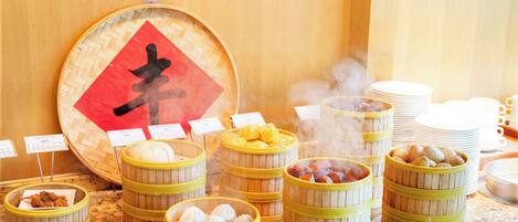 A buffet with various food items in bamboo steamers, including dumplings and corn.