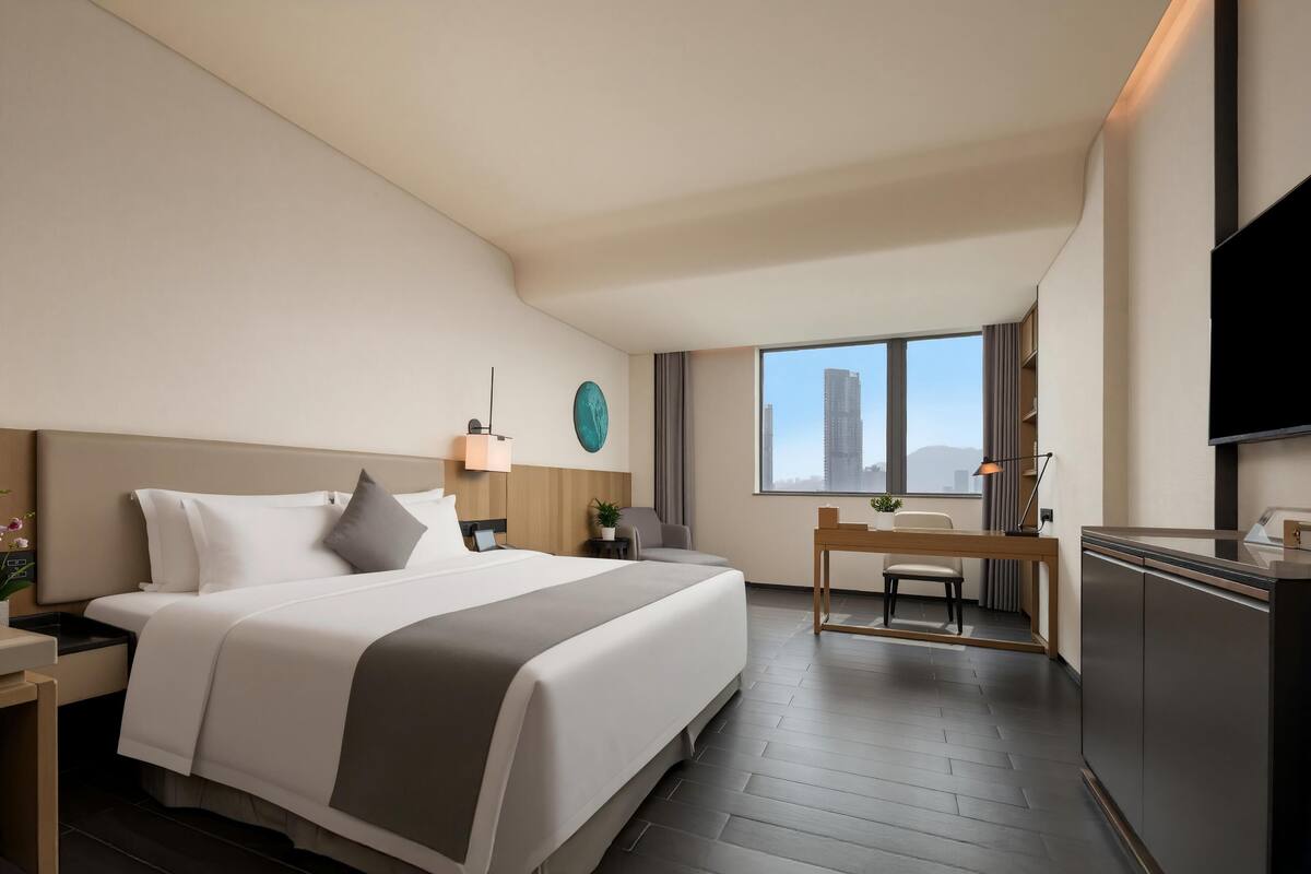 Une chambre d’hôtel moderne dotée d’un grand lit, d’un bureau, d’une télévision et offrant une vue sur la ville.