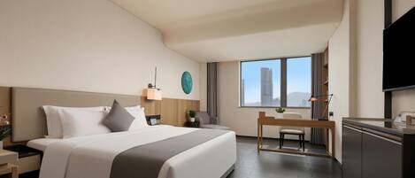 A modern hotel room with a large bed, a desk, a TV, and a view of the city.