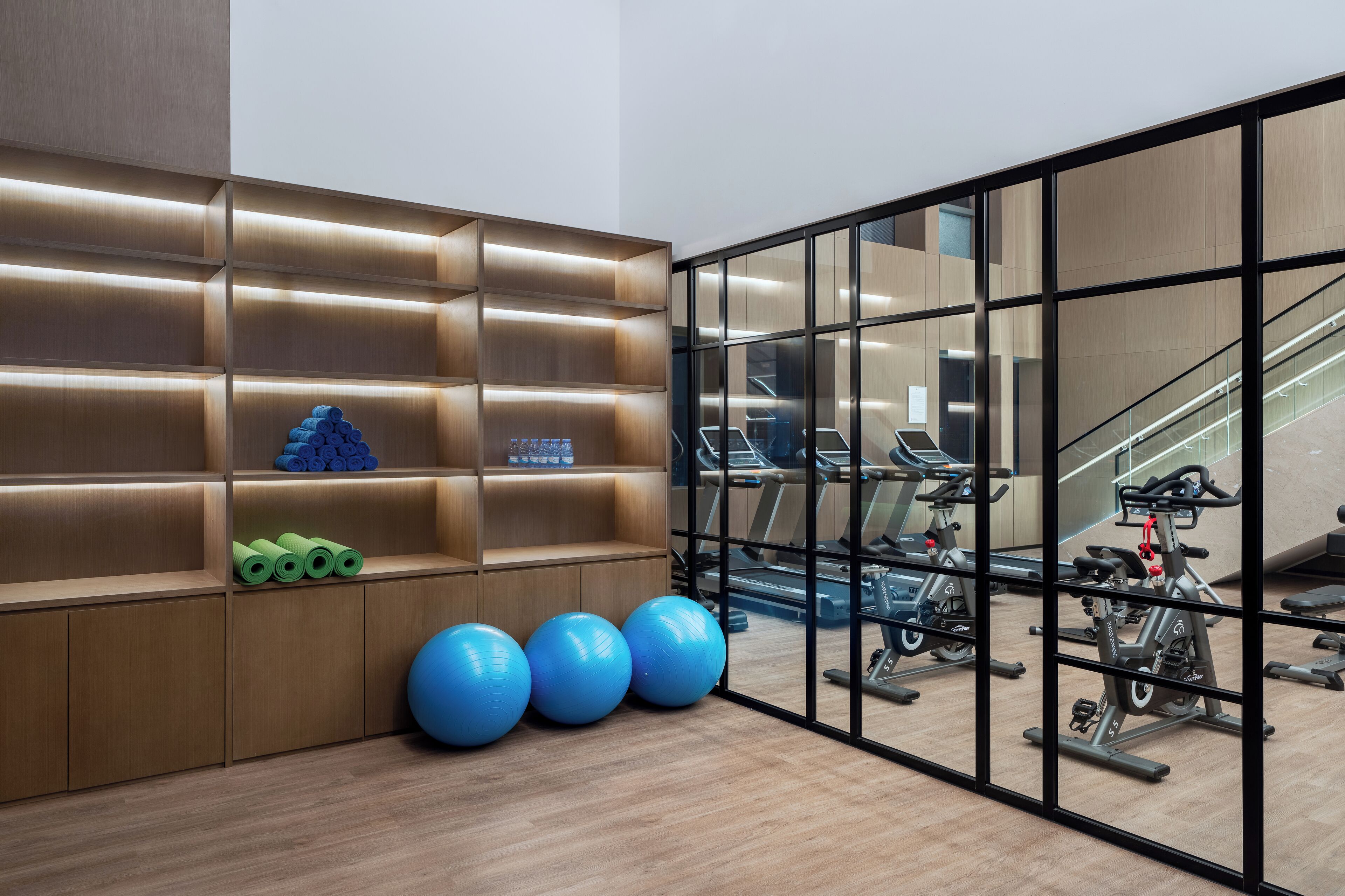 A gym with exercise equipment, a wooden wall with shelves, and a staircase.