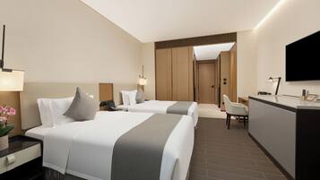 A hotel room with two beds, a desk, a chair, a TV, and a reception area.