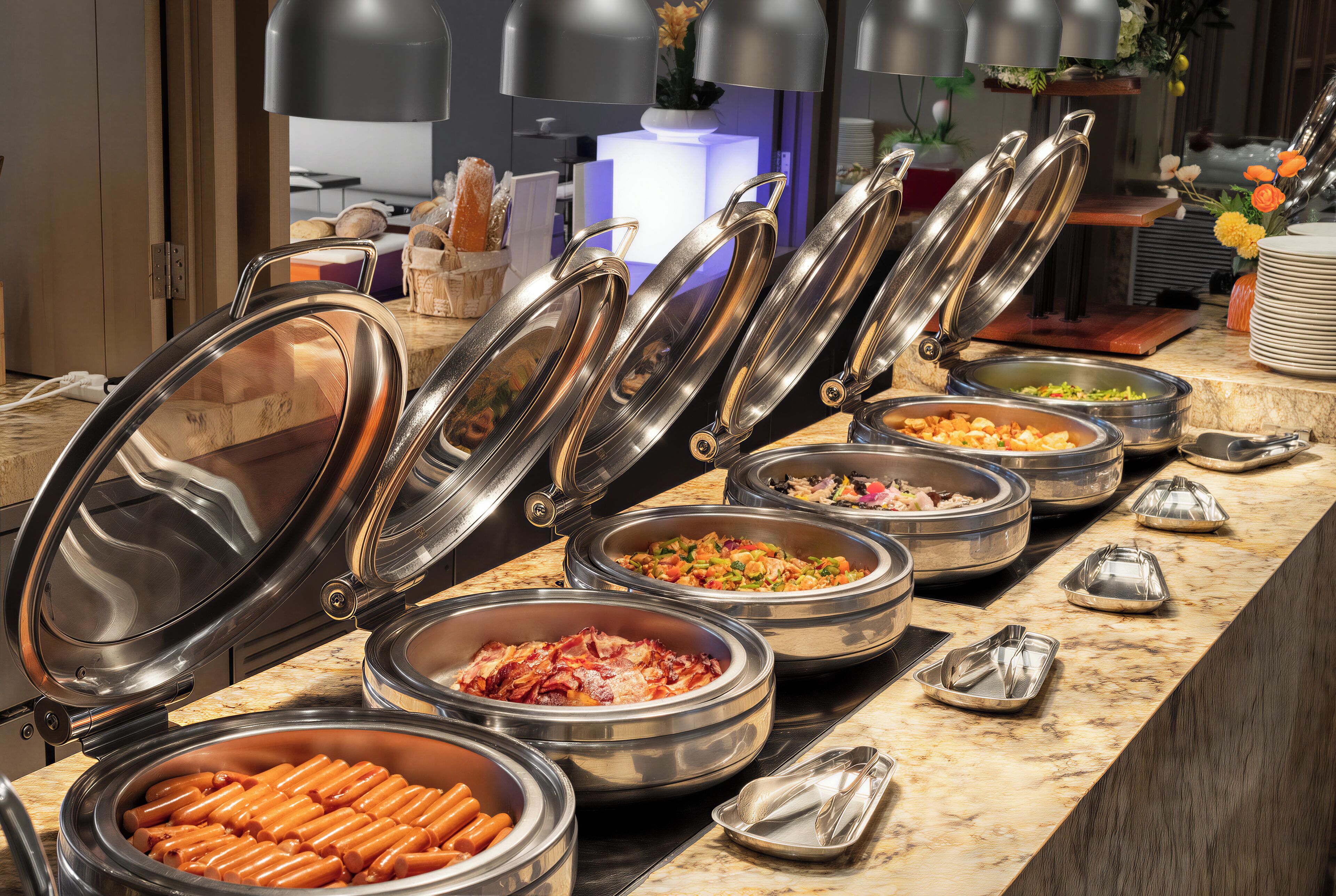 A buffet with various food items in metal serving dishes, arranged on a marble countertop.
