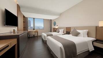 A hotel room with two beds, a desk, a TV, and a view of the city.